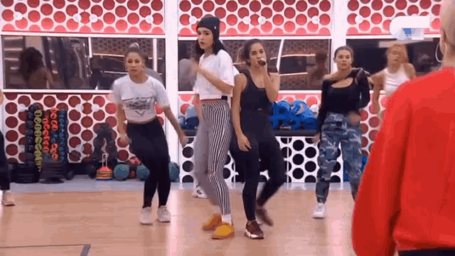 a group of women are dancing in a gym while a man in a red shirt watches
