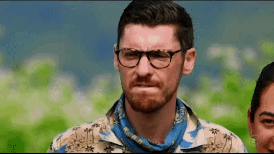 a man with glasses and a bandana around his neck is making a face .