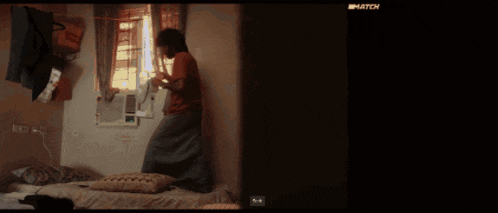 a man in a red shirt is standing on a bed in a room with a sign that says match on it
