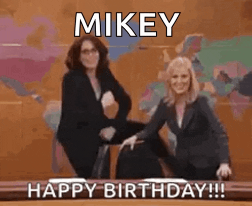 two women are dancing in front of a sign that says mikey happy birthday !!!
