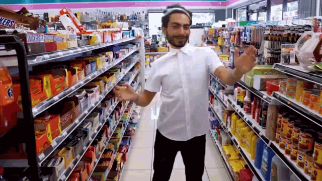 a man in a white shirt is standing in a grocery store aisle with snickers candy on the shelves