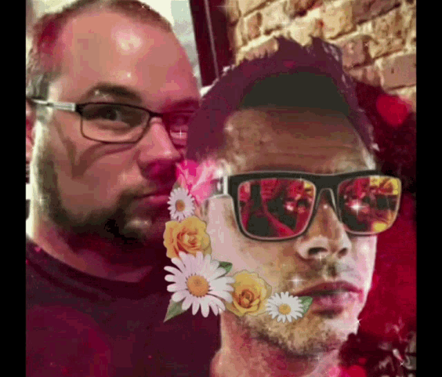a man wearing sunglasses and flowers on his face stands next to another man