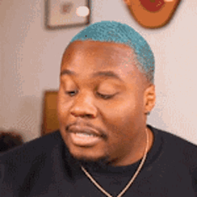 a man with blue hair and a beard is wearing a black shirt and a gold chain .
