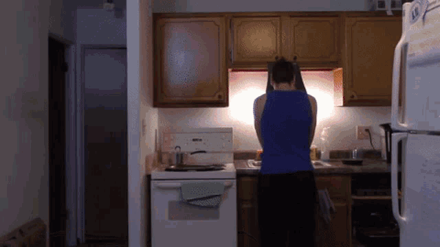 a man in a blue tank top is standing in a kitchen next to a refrigerator