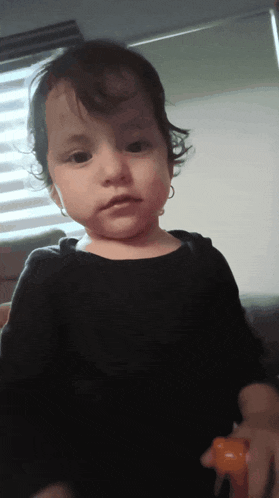 a little girl with curly hair is wearing a black shirt and earrings