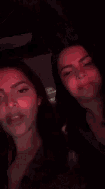 two women are laughing in a dark room with red lights