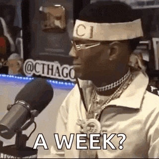 a man wearing a headband and glasses is sitting in front of a microphone and says `` a week ? ''