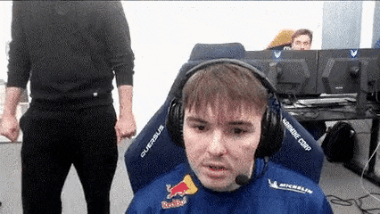 a man wearing headphones and a red bull shirt is standing in front of a computer .