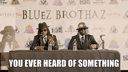 two men sitting at a table with microphones in front of a bluez brothaz banner