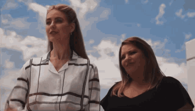 two women are standing next to each other in front of a cloudy sky