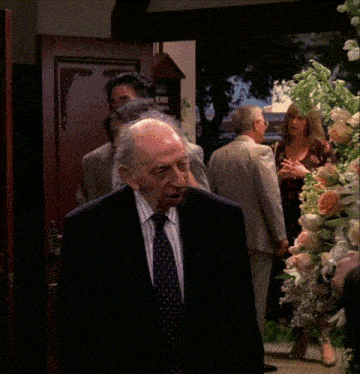a man in a suit and tie stands in front of a display of flowers