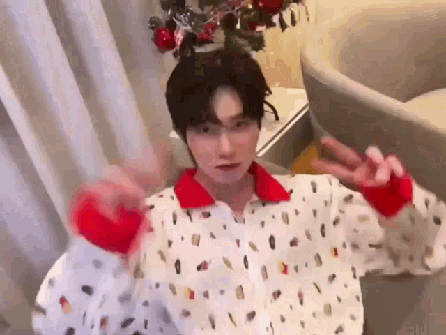a young man wearing a polka dot shirt is giving a peace sign while standing in front of a christmas tree .