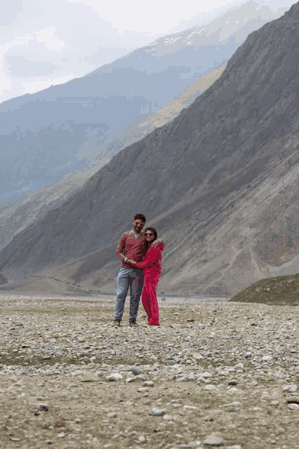 a man and a woman are posing for a picture with mountains in the background