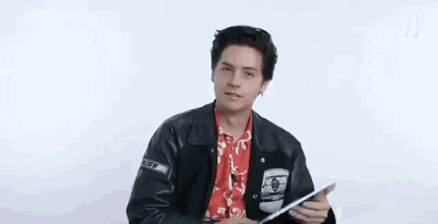 a young man wearing a leather jacket is holding a tablet .