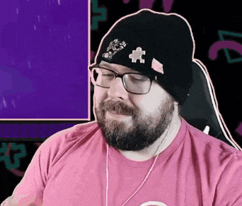 a man with a beard wearing glasses and a beanie is sitting in front of a computer screen .