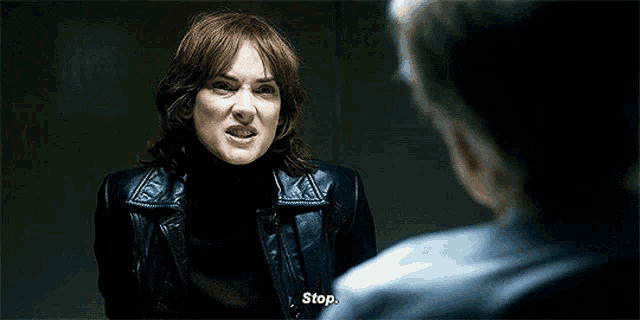 a woman in a black leather jacket is talking to a man in a blue shirt and says stop .