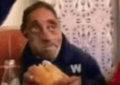 a man in a blue shirt is eating a hamburger in a restaurant .