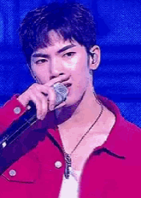 a young man is singing into a microphone while wearing a red jacket .
