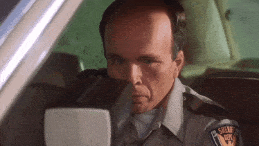 a bald man in a sheriff 's uniform is sitting in a car .