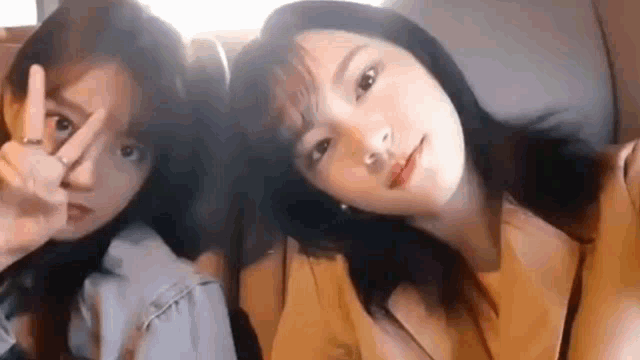 two women are sitting next to each other and making a peace sign with their hands .