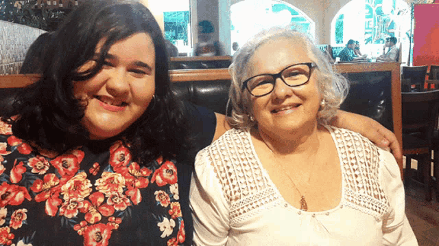 two women posing for a picture with one wearing glasses and a floral top