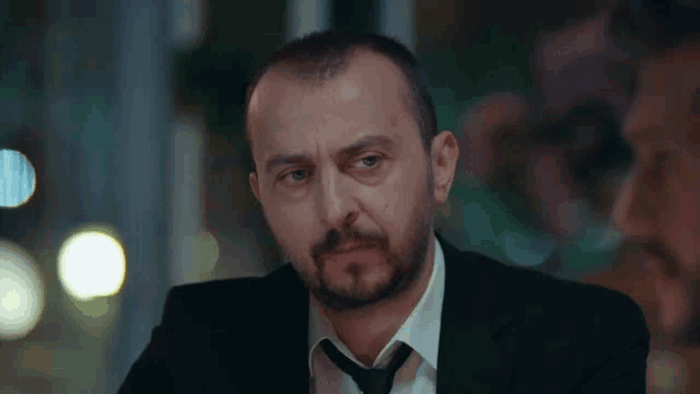 a man with a beard wearing a suit and tie looks at the camera
