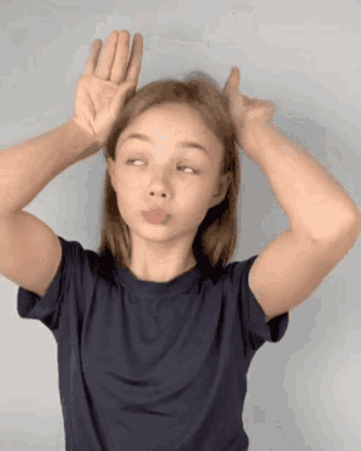 a young girl in a blue shirt is making a funny face with her hands on her head