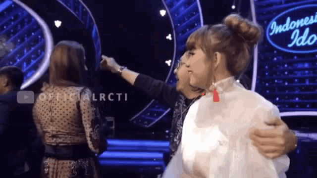 two women are hugging in front of an indonesia idol sign