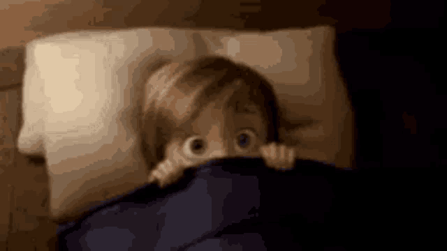 a child is peeking out from under a blanket in bed .
