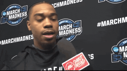 a man is speaking into a microphone in front of a march madness sign