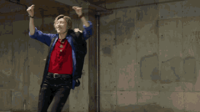a man in a red shirt and a blue jacket is dancing in front of a concrete wall