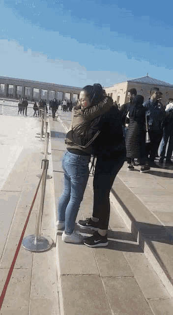 two women hugging each other on a sidewalk in front of a building