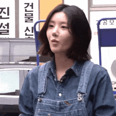 a woman wearing overalls stands in front of a sign that says ' korean '