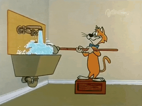 a cartoon cat is standing on a box next to a sink holding a mop .