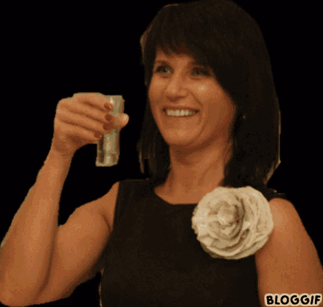 a woman in a black dress with a flower on her shoulder is holding a drink