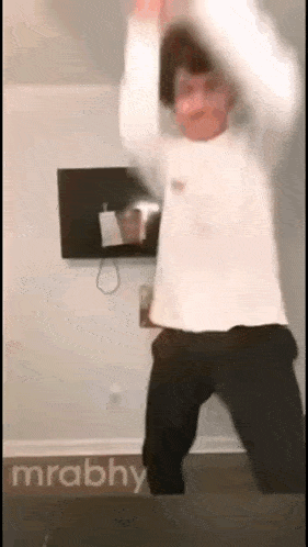 a man in a white shirt and black pants is jumping in the air in a living room .