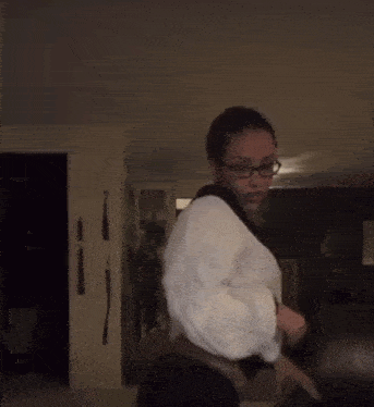 a woman in a taekwondo uniform is dancing in a dark room .