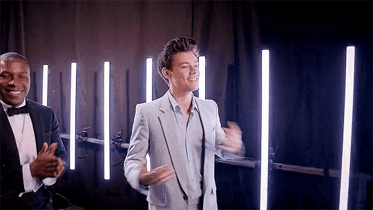 a man in a suit is dancing in front of a microphone while another man applauds .
