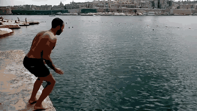 a man is jumping into a body of water with a city in the background