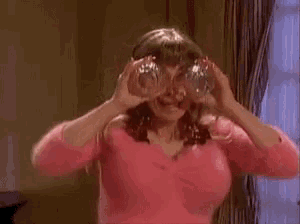 a woman in a pink top is holding a pair of binoculars in front of her eyes .