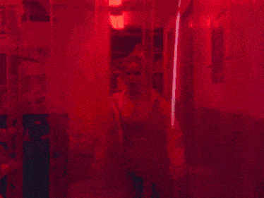 a woman wearing headphones and a pink jacket stands in front of a red curtain