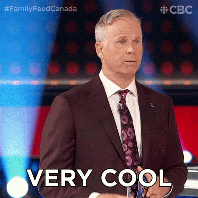 a man in a suit and tie says " very cool " while standing on a stage