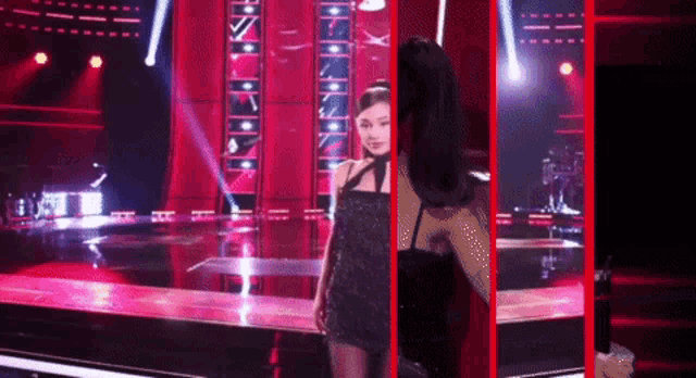 a woman in a black dress stands on a stage with a red background