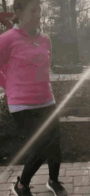 a woman in a pink sweater and black pants is walking on a sidewalk