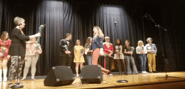 a group of people standing on a stage with a woman holding a microphone