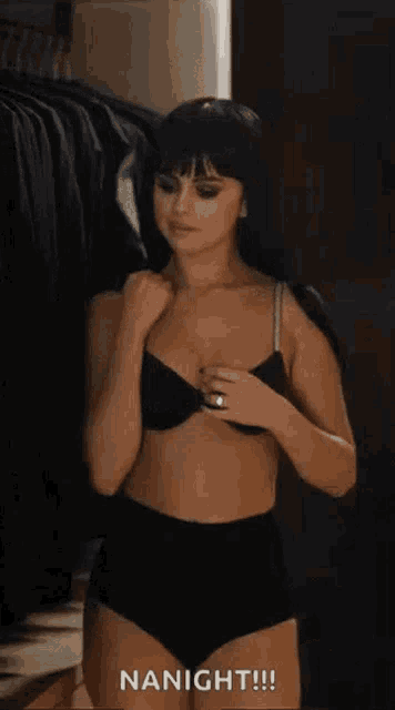 a woman in a bra and panties is standing in a room holding a cigarette .