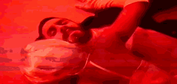 a man is laying on the floor in a red light with a plastic bag around his neck .