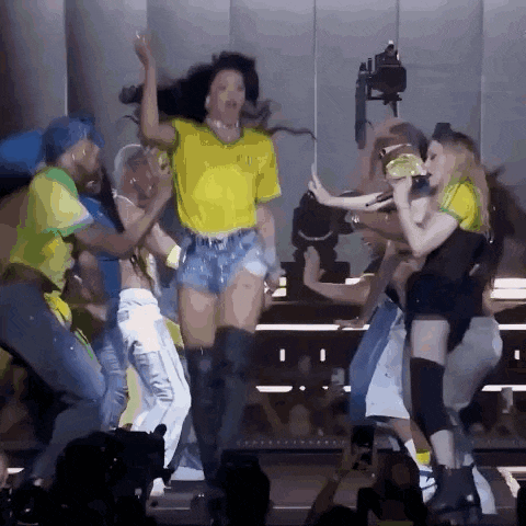 a woman in a yellow shirt is surrounded by a group of people on a stage