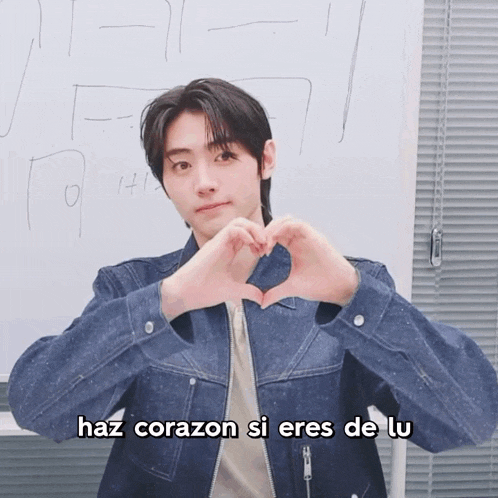 a man in a denim jacket making a heart with his hands