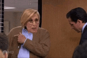 a man and a woman are standing next to each other in an office and the woman is pointing at the man .